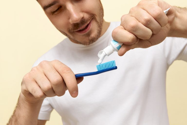 cropped-shot-cheerful-healthy-young-caucasian-man-white-t-shirt-squeezing-paste-toothbrush-brushing-teeth-after-waking-early-morning-min
